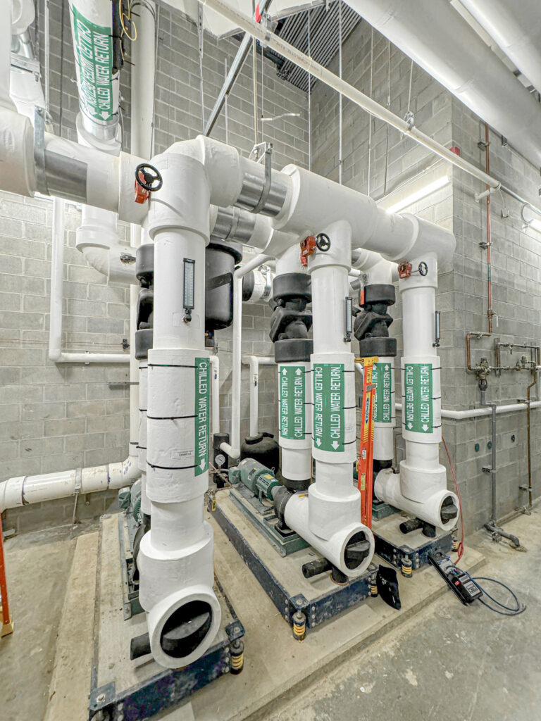 Chilled water return system with insulated pipes, valves, and pumps in a mechanical room, part of an HVAC system for commercial cooling